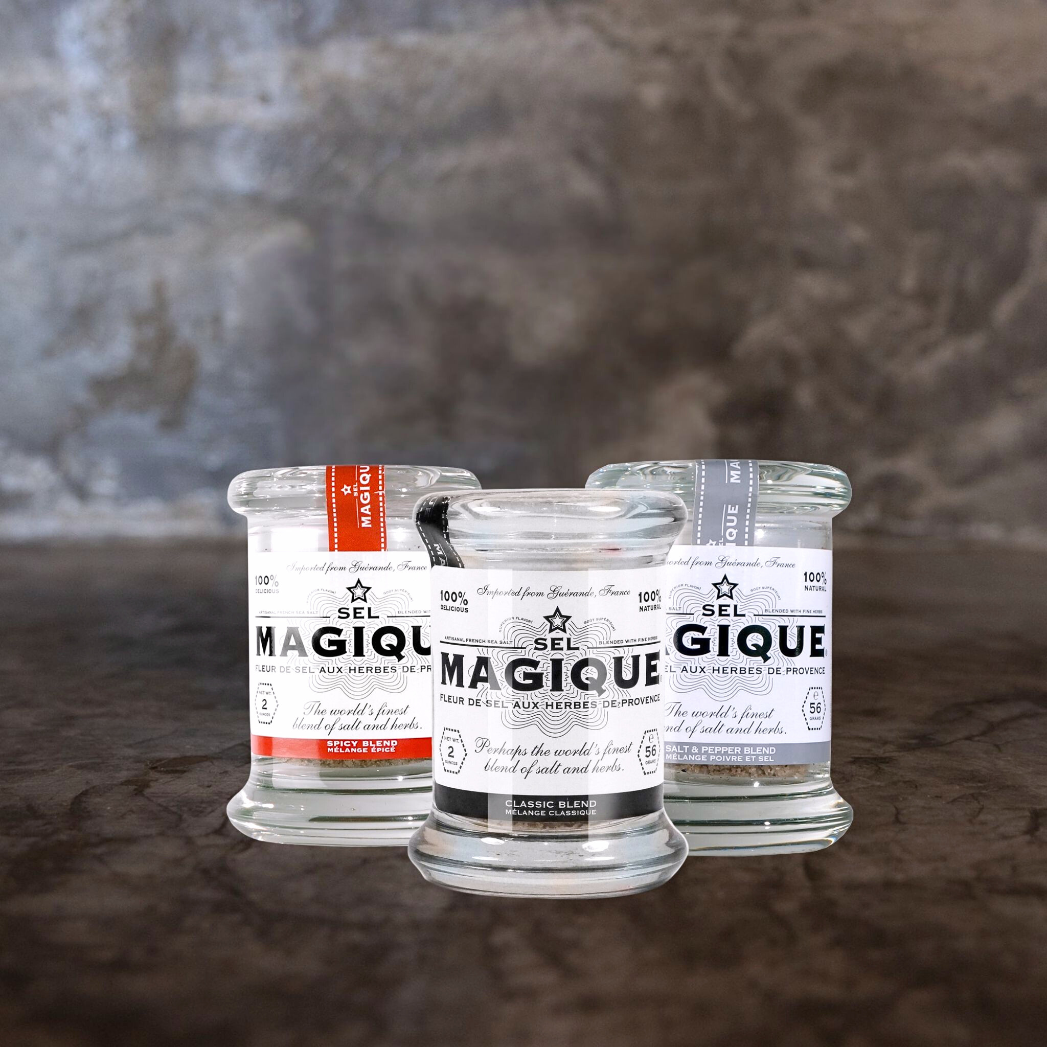 Three jars of 'Sel Magique' on a textured surface with a gray background